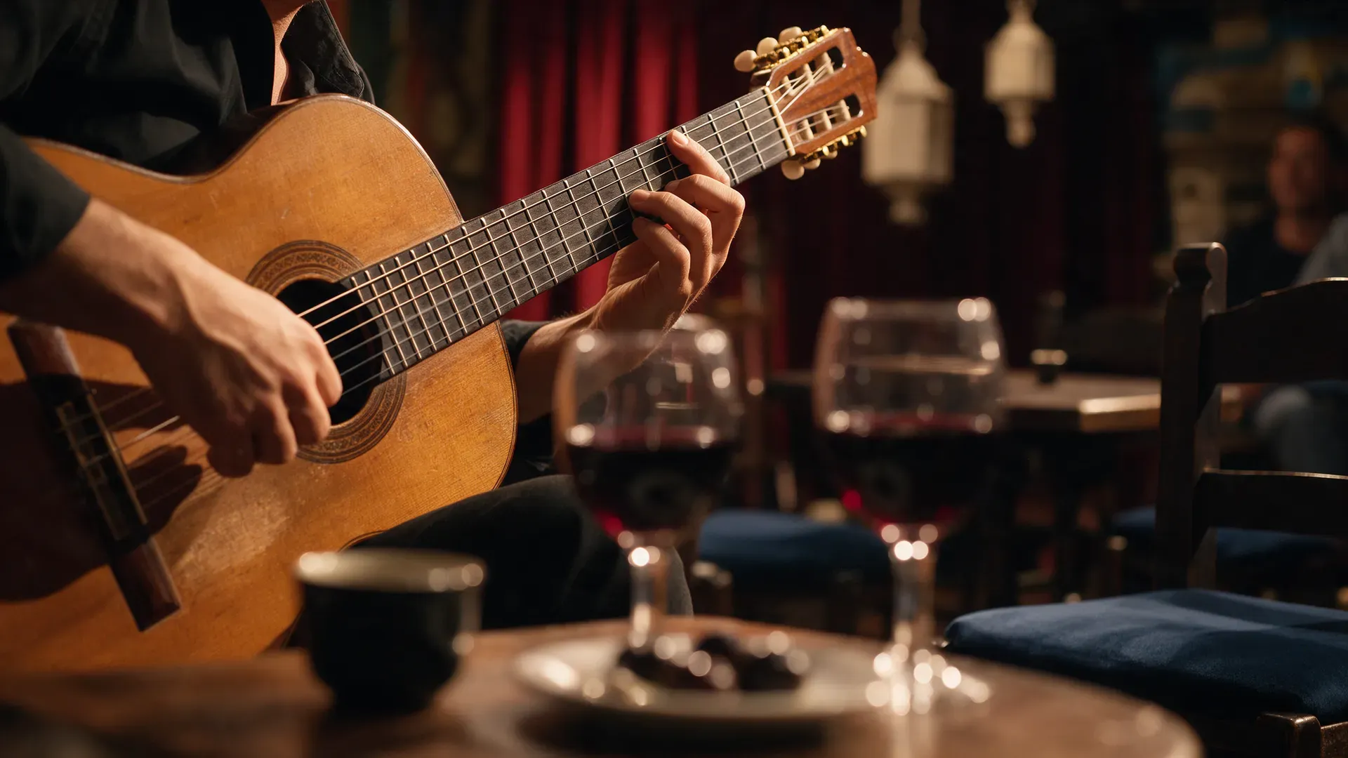 A flamenco guitarist's hands on the strings in warm stage light, glasses of wine on a table in the foreground